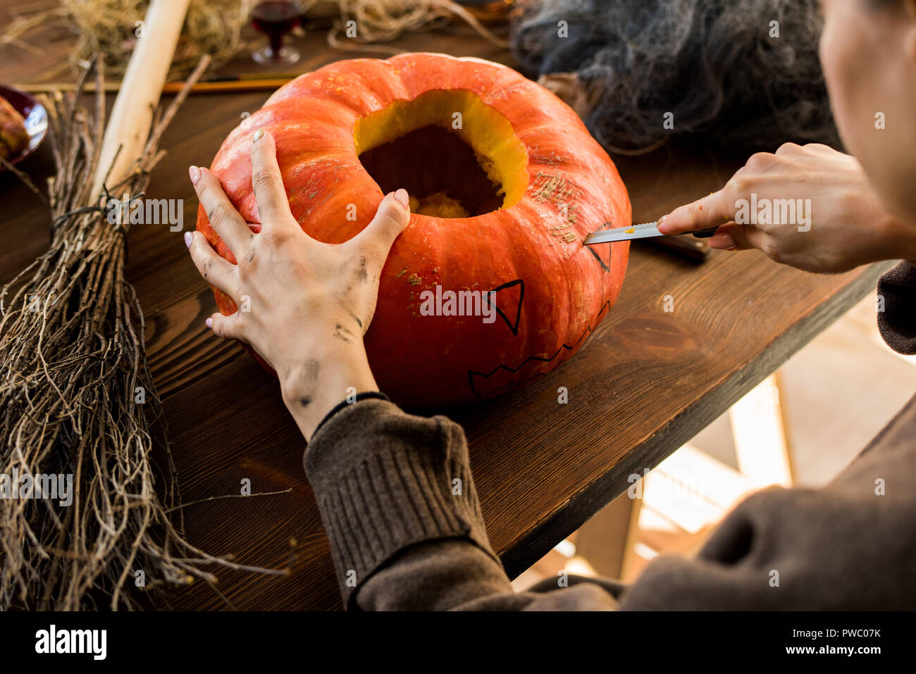 Nahaufnahme der unkenntlich Frau sitzt am Tisch und schneiden Auge auf Kürbis während Jack-o-Lantern in Werkstatt Stockfoto