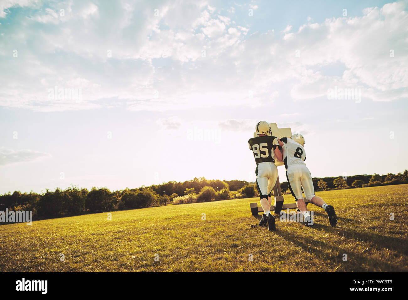 Zwei American Football Spieler tun Angriff Bohrer mit einem Angriff Schlitten außerhalb auf einem Sportplatz bei einem Nachmittag Praxis Stockfoto