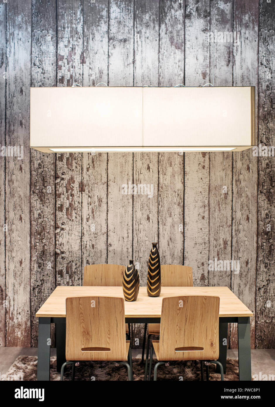 Moderne Holztisch und Stühlen mit stilvollen Keramik Vasen durch eine rechteckige Decke Licht vor einem rustikalen hölzernen Wand beleuchtet eingestellt Stockfoto