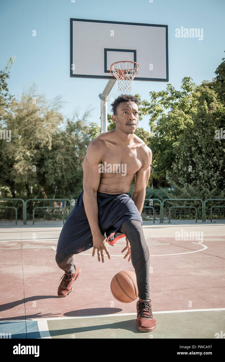 Eine afroamerican junger Mann ohne T-Shirt ist Basketball spielen in einem  Park in Madrid im Sommer mittags. Er springt die Kugel unter dem Korb  Stockfotografie - Alamy