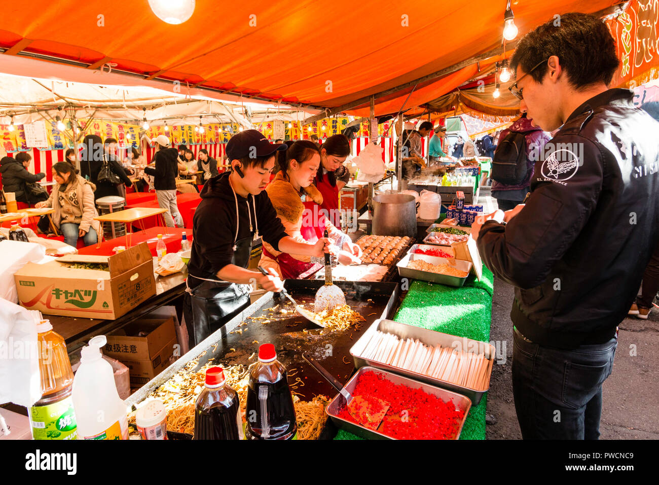 Japanische junge mand und zwei junge Frauen, bei Yakisoba takeaway Kochen gebratene Buchweizennudeln auf Warmhalteplatte während des Festivals. Kunde wartet. Stockfoto