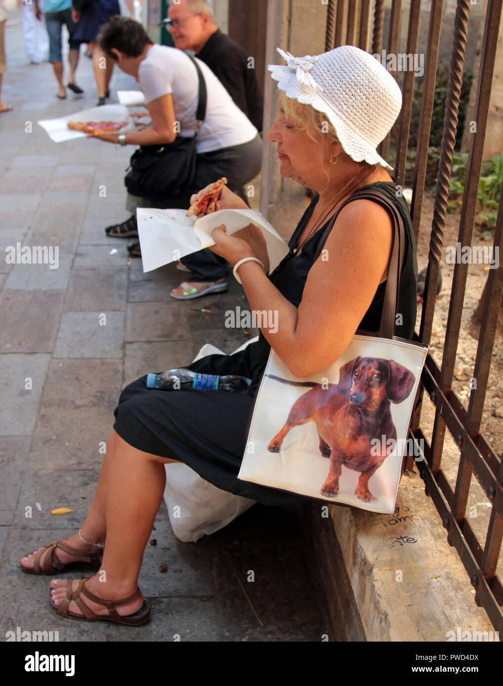 Eine Frau sitzt auf einer Wand genießen Sie ein Stück Pizza. Sie hat ihr Doggy Bag bereit, wenn Sie nicht die Schicht zu beenden. Stockfoto