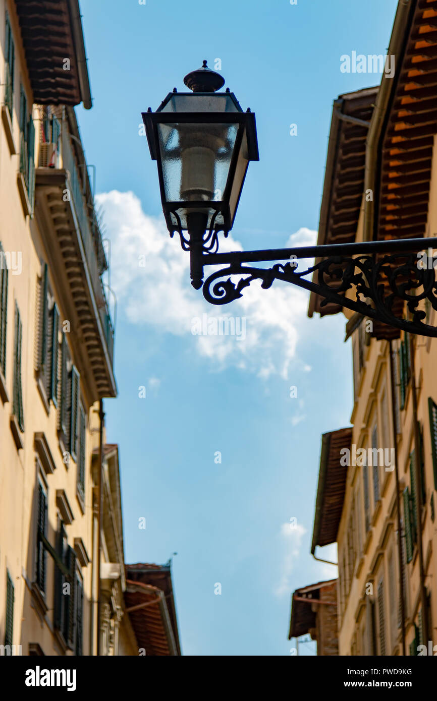 Eine Straßenleuchte ragt zwischen zwei Gebäuden und ist gegen einen blauen Himmel in einer Gasse in Florenz, Italien, Silhouetted Stockfoto