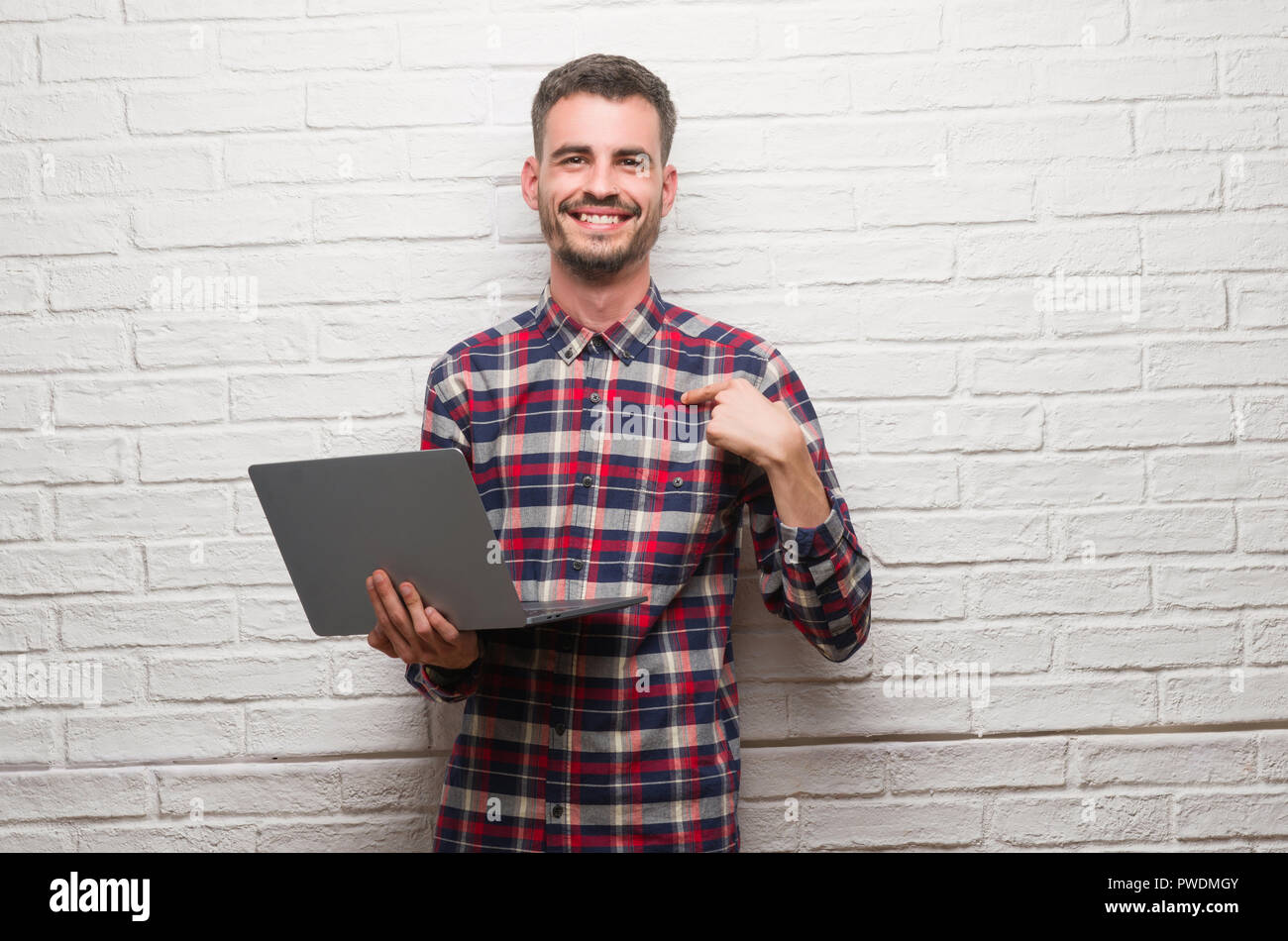 Junger Erwachsener Mann mit Laptop mit Überraschung Gesicht zeigenden Finger zu sich brick wall Stockfoto