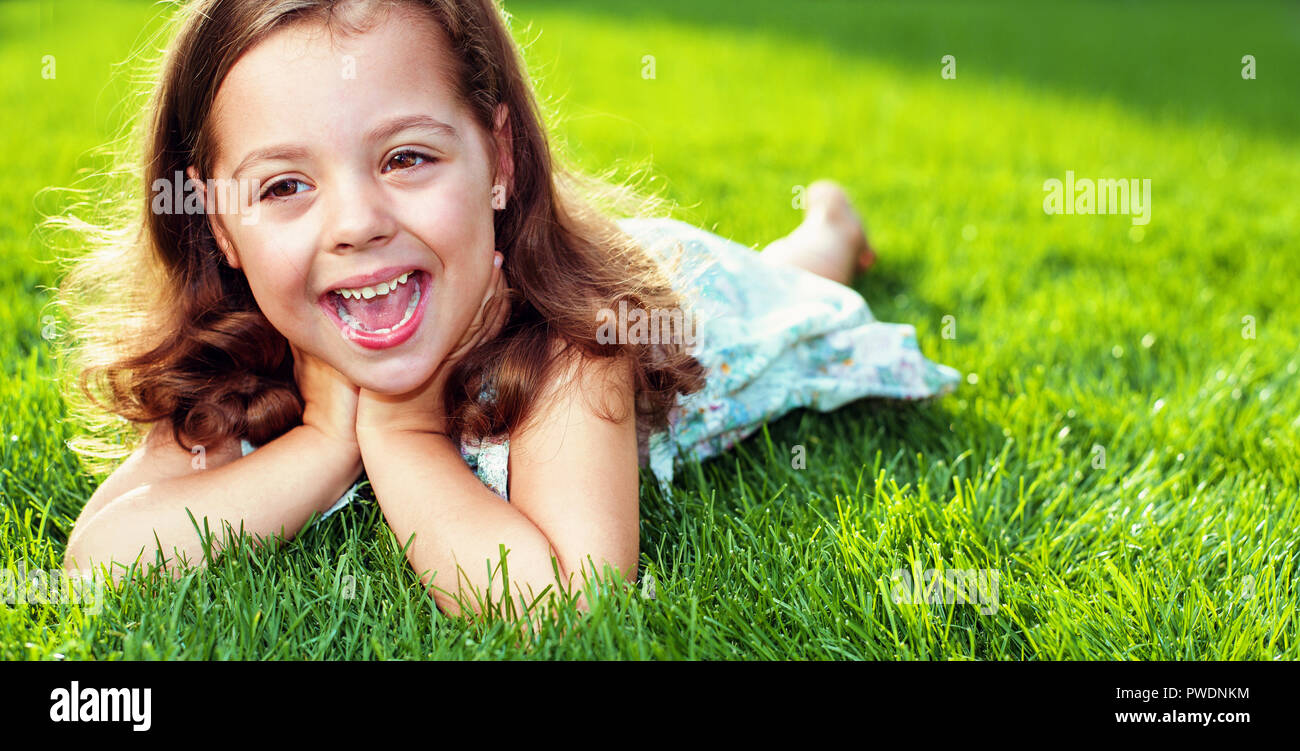 Süße kleine Mädchen, die auf eine warme, frische grüne Wiese Stockfoto
