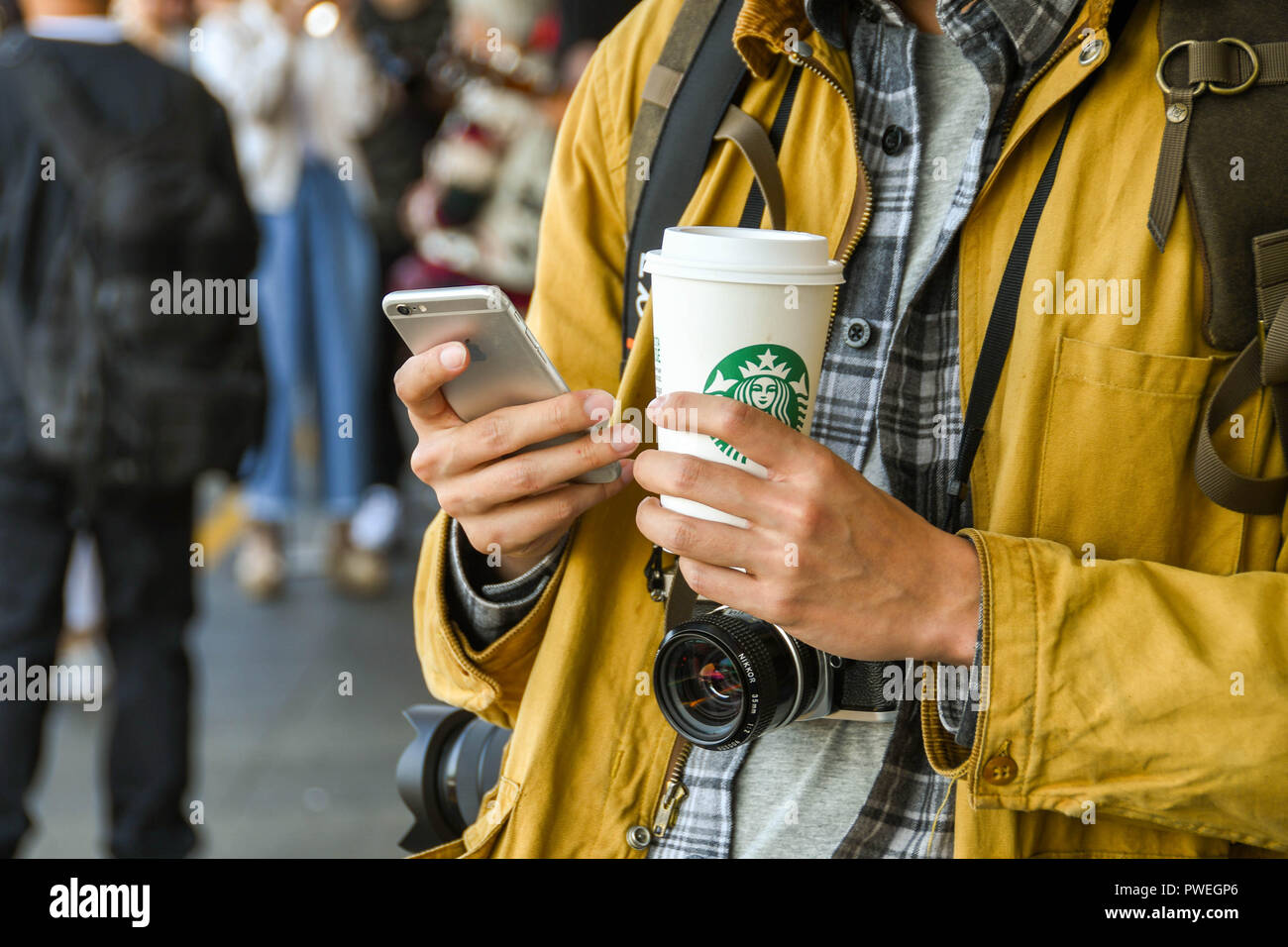 SEATTLE, WASHINGTON STATE, USA – JUNI 2018: Nahaufnahme eines Touristen mit einer Kamera, die SMS auf einem Telefon sendet und eine Tasse Starbucks-Kaffee in der Hand hält Stockfoto