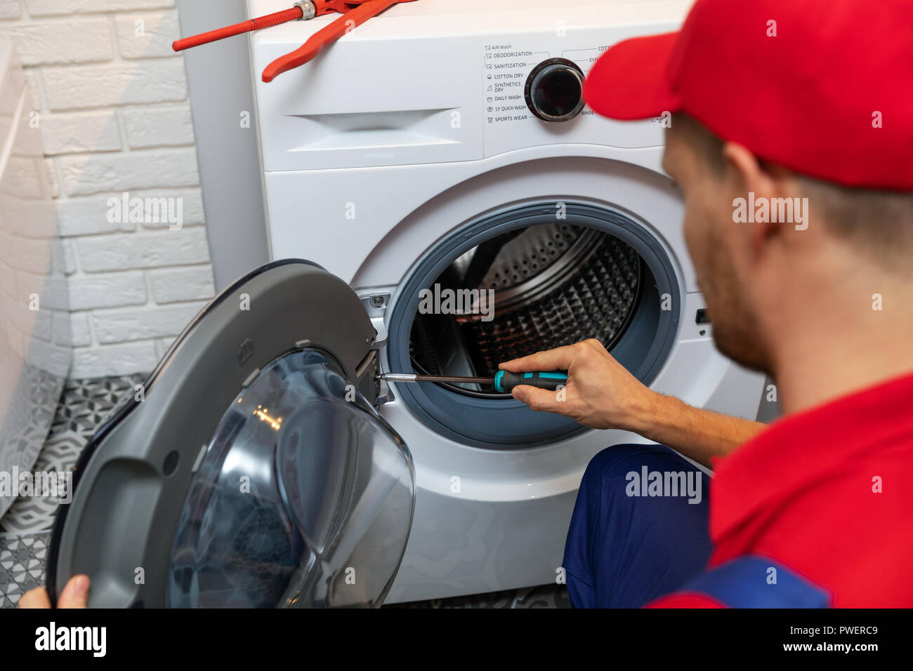 Handwerker mit Schraubendreher Reparatur Waschmaschine Tür Stockfoto