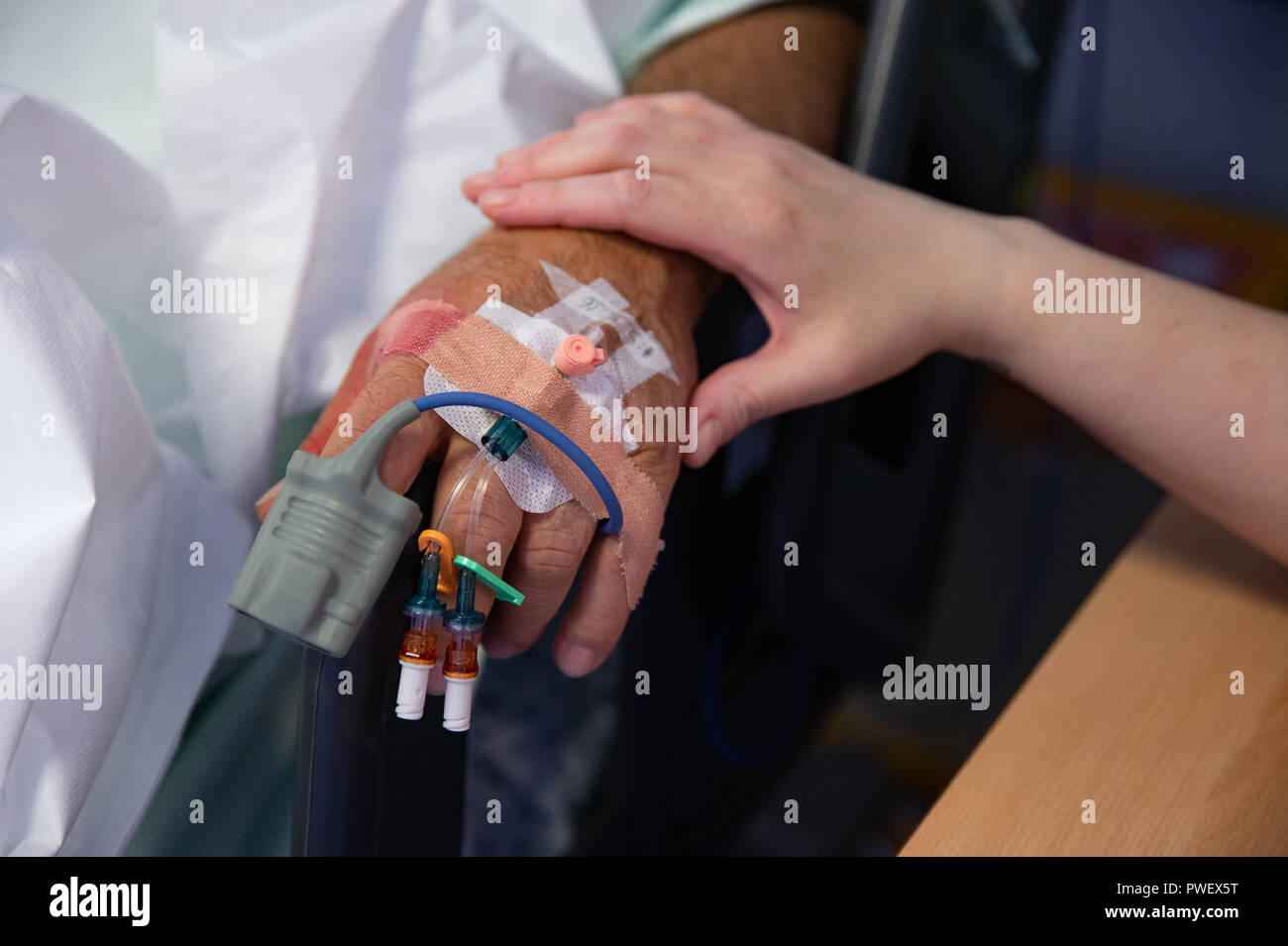 Nahaufnahme der Hand eines NHS-Patienten auf eine Infusion mit einer stützenden Hand einer Krankenschwester Stockfoto