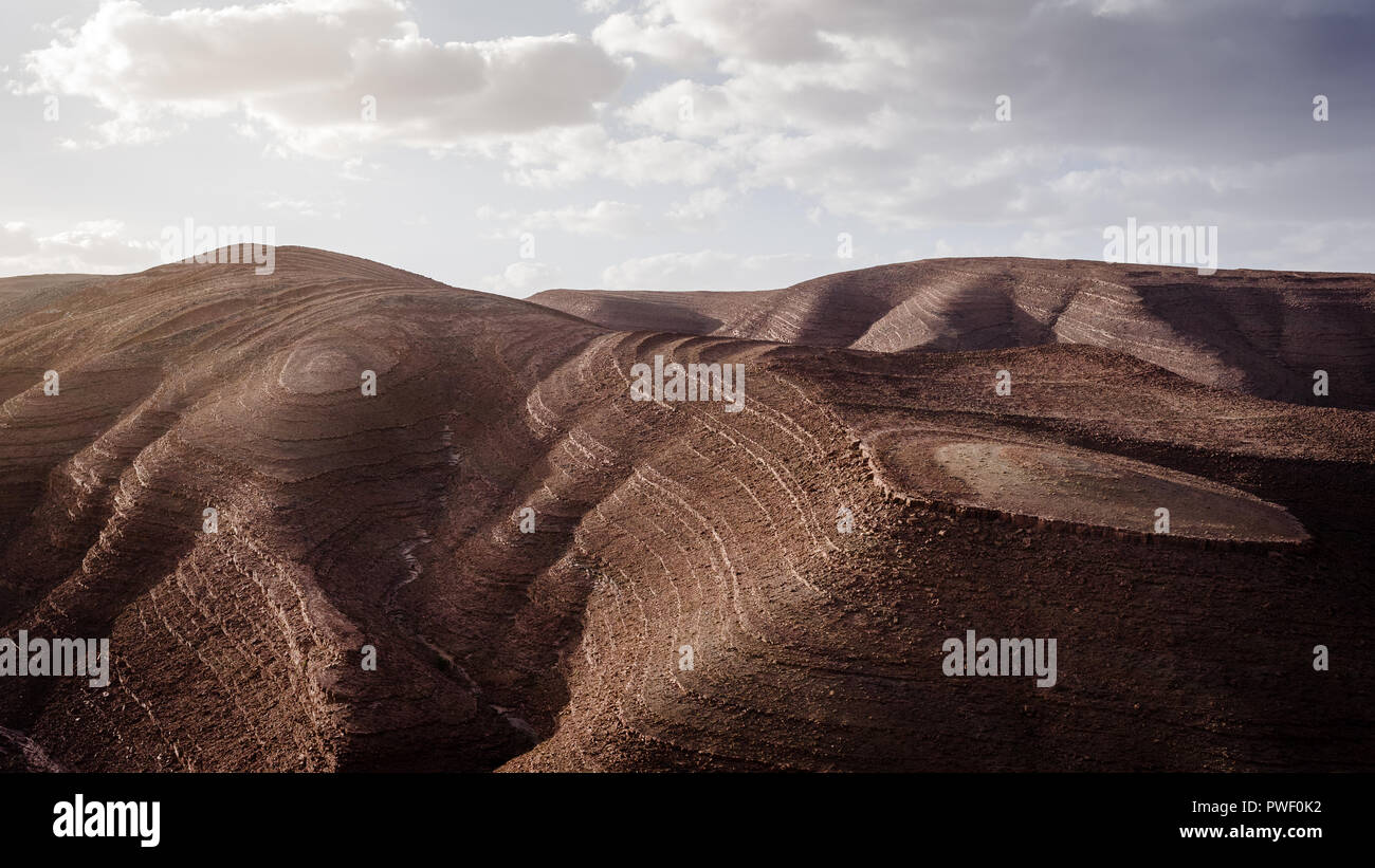 Surreale braunen Landschaft im Atlasgebirge in Marokko mit bewölktem Himmel und strahlendem Sonnenschein Stockfoto