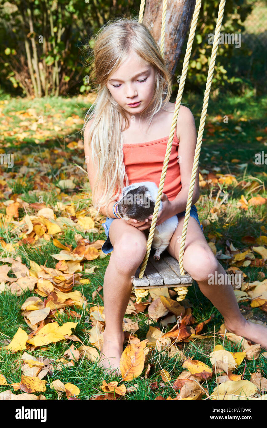 Niedliche kind Mädchen sitzen auf Schaukel im Garten und spielt mit Meerschweinchen Haustier Stockfoto