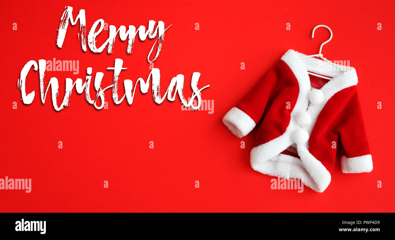 Frohe Weihnachten weißer Text und Santa Claus (Sankt Nikolaus) mini Mantel Anzug Kostüm mit weißer Kleidung Manschetten auf ein leuchtend roter Hintergrund isoliert. Konzept Stockfoto
