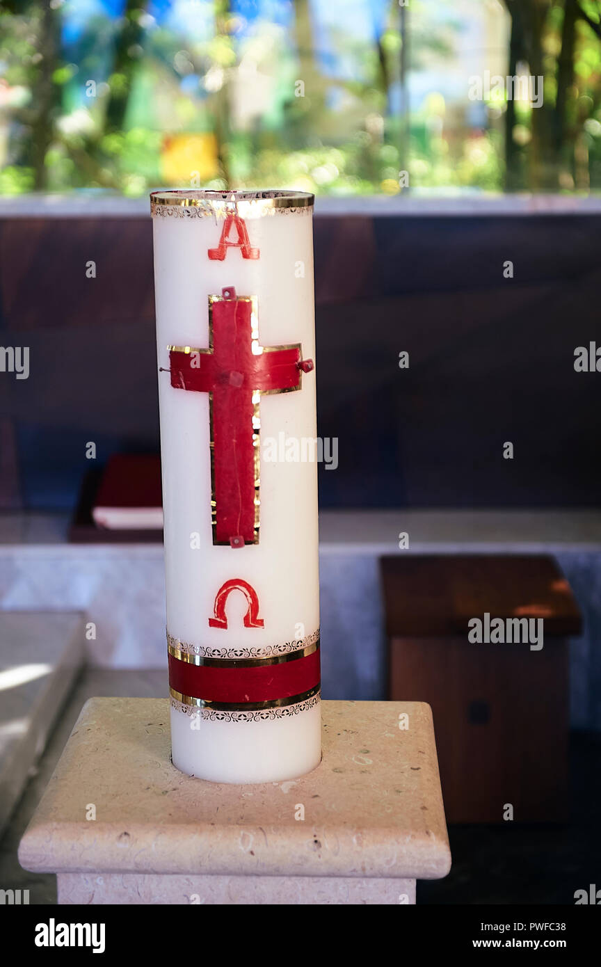Osterkerze an der Kath. Kirche, zeigt das Kreuz in Rot und Gold, und die griechischen Buchstaben Alpha und Omega Stockfoto