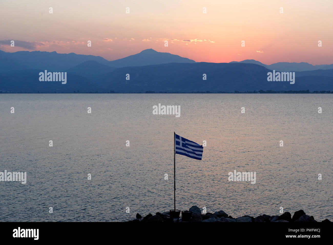 Dämmerung Blick auf eine griechische Flagge mit Blick auf die Hügel und die Gewässer der Umgebung der Stadt Nafplio. Peloponnes. Griechenland. Stockfoto