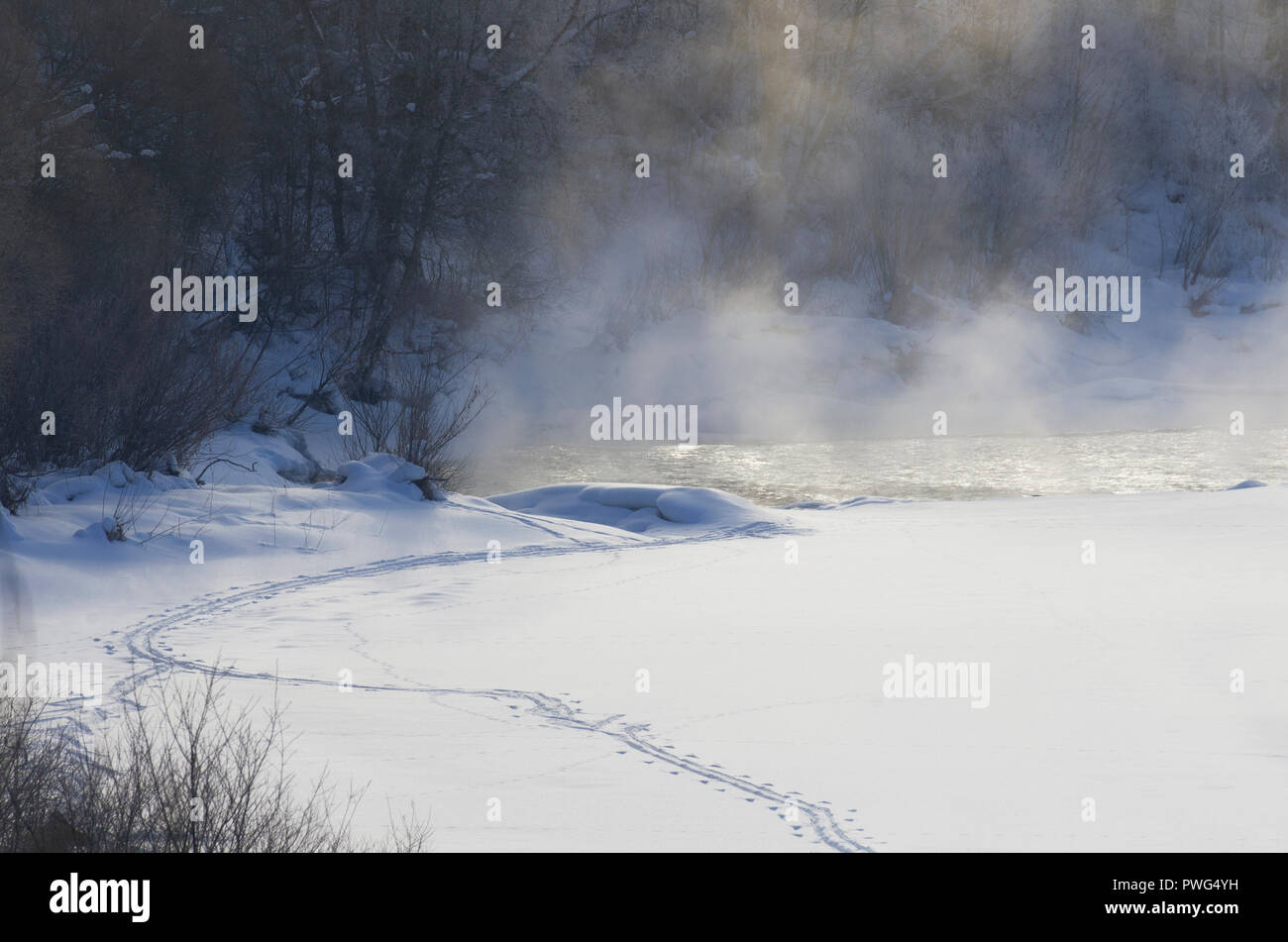 Nebel über dem Fluss an einem frostigen Morgen mit einem Pfad auf weißem Schnee im Winter Stockfoto