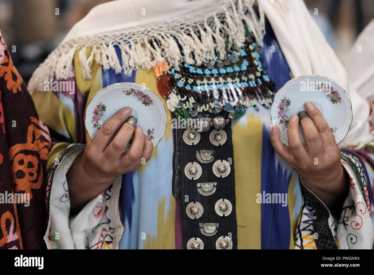 Usbekische Frau, die traditionelle Kleidung aus der Region Buchara mit Kaffee Untertassen und Metall nähen Fingerhüten an den Fingern für Percussion während des Bukharian Kaffee Untertasse Tanz. Usbekistan Stockfoto