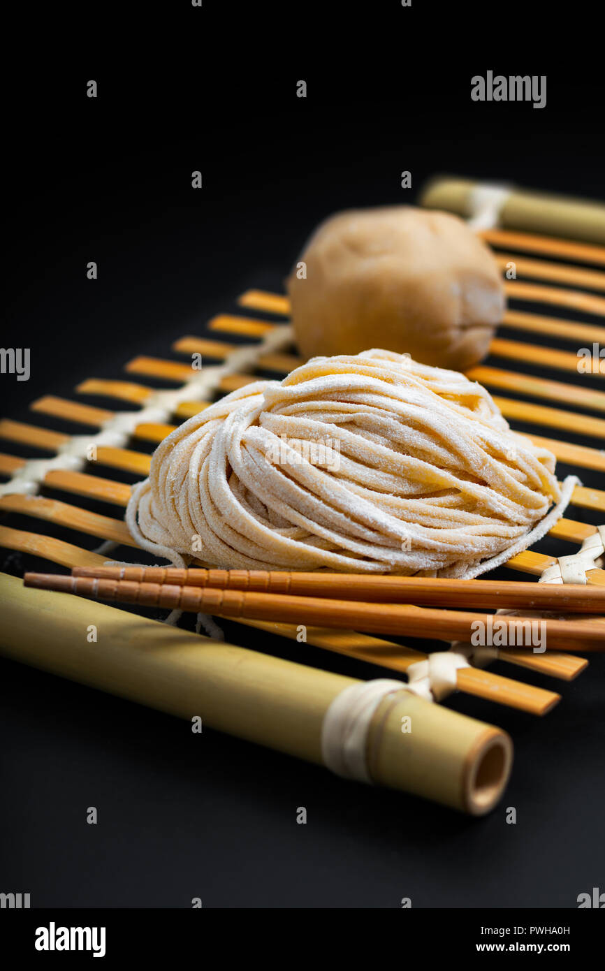 Essen frische rohe Hausgemachte orientalische asiatische, chinesische Eiernudeln durch organische Eier und Mehl halbweiss auf einem Bambus Fach Stockfoto