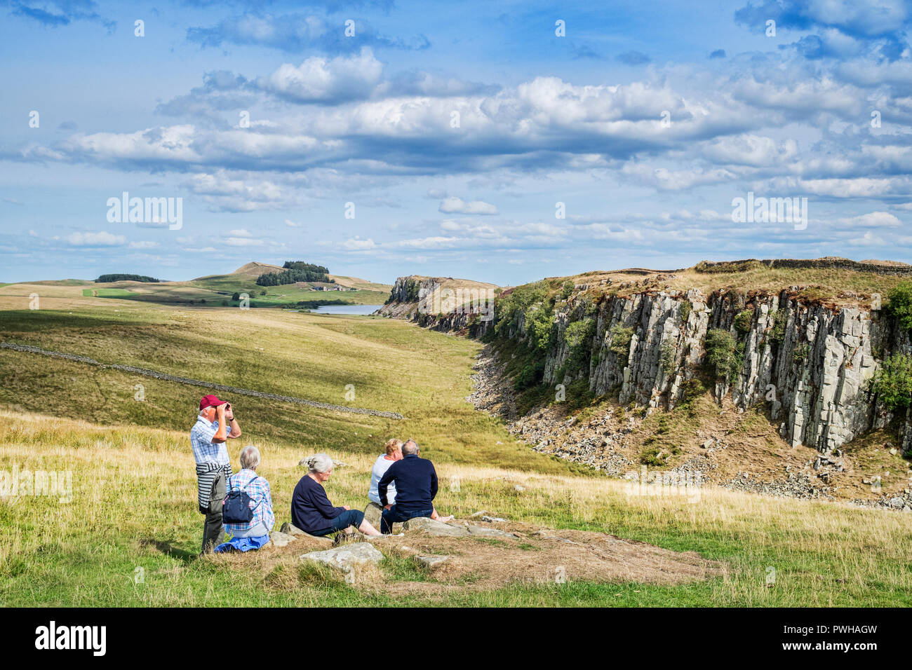 11. August 2018: Hadrian's Wall, Northumberland, Großbritannien - Gruppe von grauen Haaren Senioren sitzen auf dem Gras an walltown Crags. Stockfoto