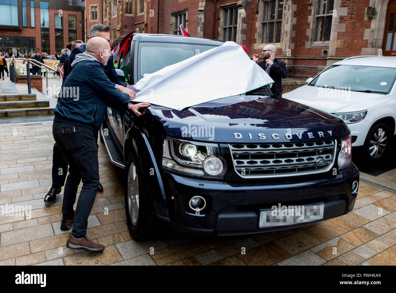 Anmerkung des Editors: NUMMERNSCHILD PIXELATED DURCH PA BILD SCHREIBTISCH einen Security Officer (teilweise verdeckt) Entfernt eine Fahne auf dem Fahrzeug des israelischen Botschafters in das Vereinigte Königreich Mark Regev, als er nach dem Besuch der Queen's University in Belfast fährt. Stockfoto