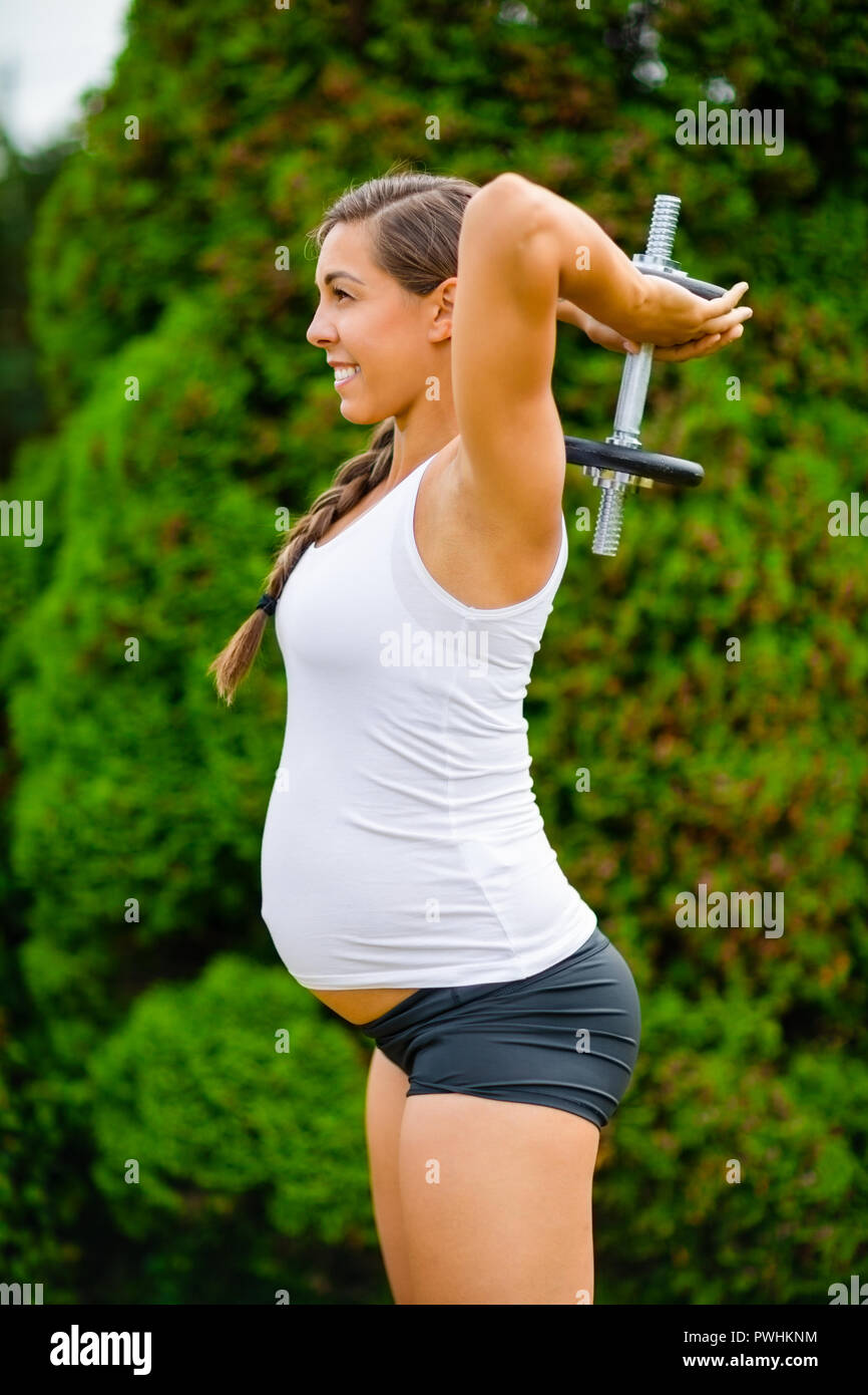 Zuversichtlich werdende Mutter tun overhead Trizeps Erweiterungen mit Hantel in Park Stockfoto