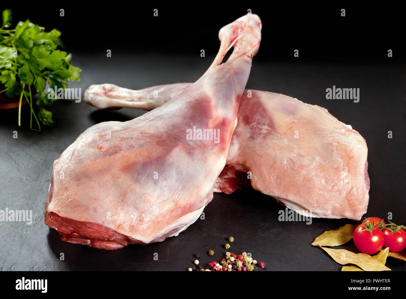 Frisch und rohes Fleisch. Lammkeule rohe Tomaten und Paprika auf schwarzem Hintergrund Stockfoto