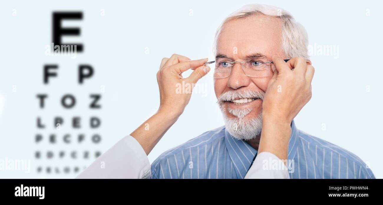 Gerne älterer Mann heraus versuchen, neue Lesebrille, auf Hintergrund Auge Diagramm. Reifer Mann mit neuen Gläser nach Eye Exam Stockfoto
