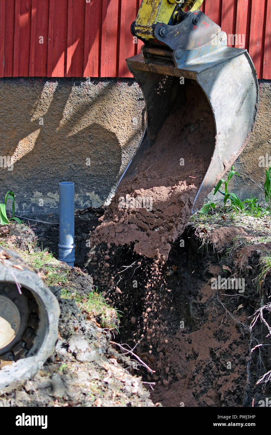 Bagger in Baustelle füllen das kanalrohr Graben mit Sand. Bild vertikal. Stockfoto