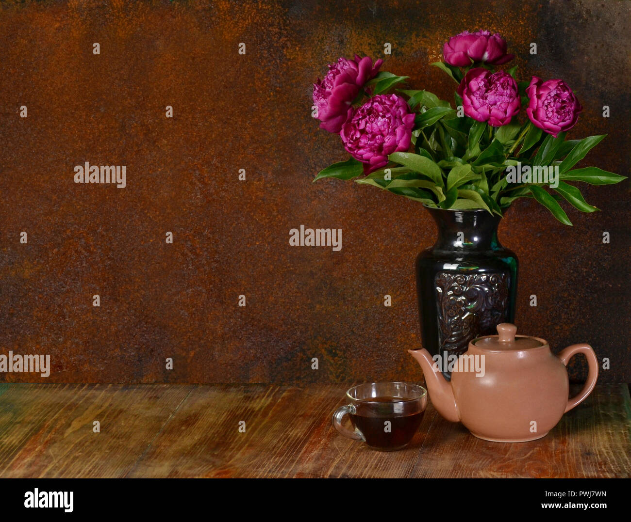 Schönen lila Päonien in eine Vase, eine Tasse Tee und ein Wasserkocher auf einer rostigen Hintergrund. Stockfoto