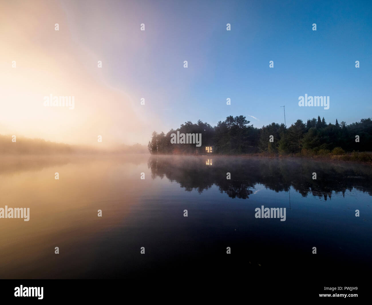 Ein Haus am See am See Benoir in Dysart et. al., Ontario, Kanada während einer nebligen Herbst morgen mit Sonne von Links Stockfoto