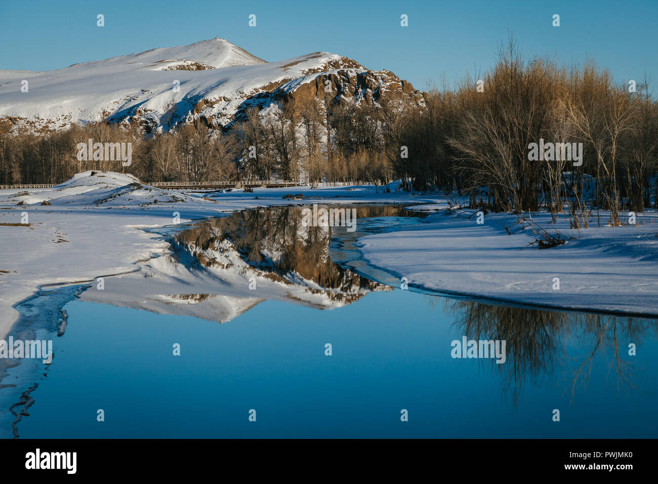 Snowy Mongolische Landschaft, Reflexion der schneebedeckten Berge, Bäume und blauer Himmel in einem eisigen Fluss. Arkhangai, Mongolei Stockfoto