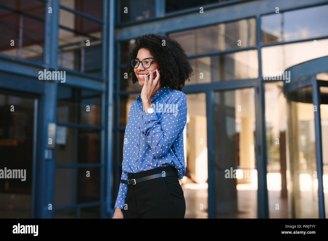 Junge Geschäftsfrau zu Fuß aus dem Bürogebäude Gespräch am Handy. Weibliche Büroangestellte zu Fuß aus dem Firmengebäude der Ph Stockfoto