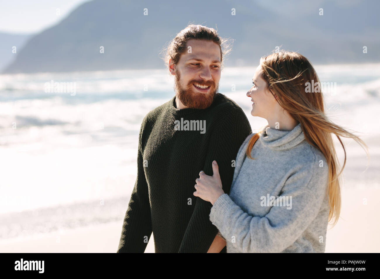 Schöner Mann zu Fuß mit seiner Freundin am Strand. Junges Paar zusammen entlang der Küste. Stockfoto