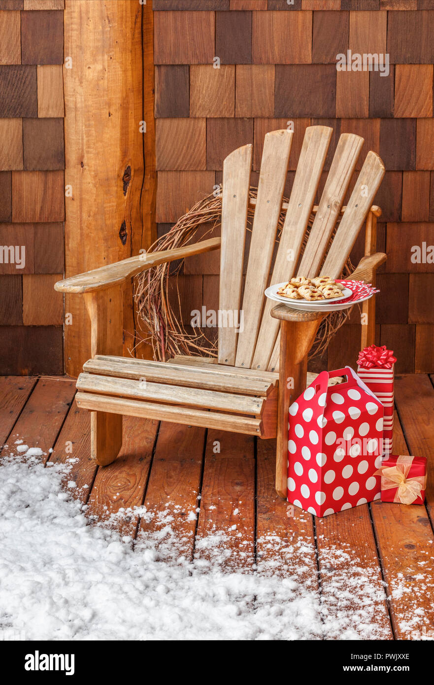 Adirondack Stuhl mit Weihnachten Geschenke und Cookies auf dem verschneiten Veranda eines rustikalen Hütte. Winterurlaub Ferienhaus getaways Retreats. Stockfoto