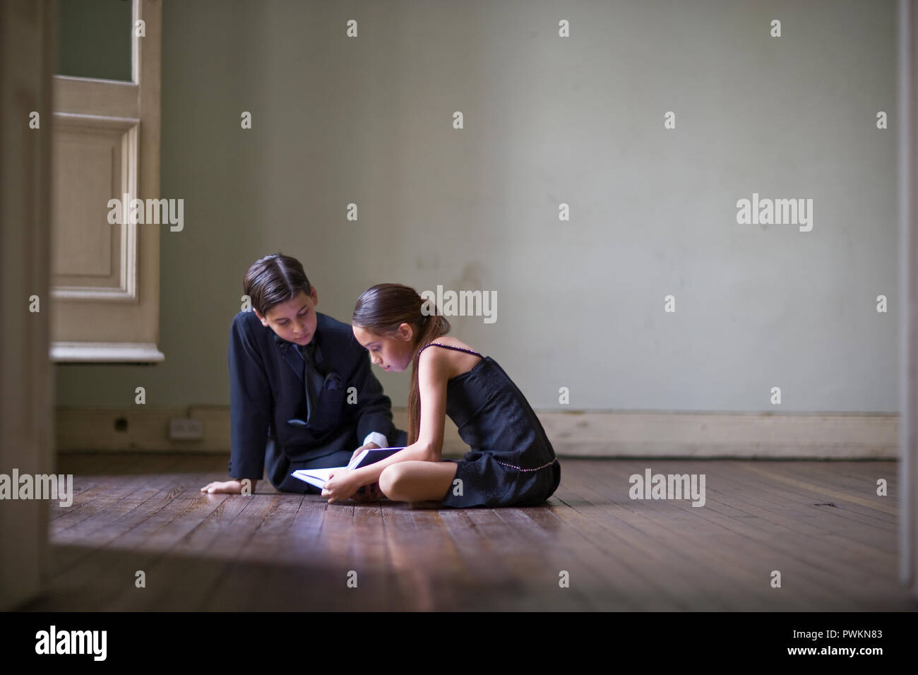 Mädchen lesen ein Buch mit ihrem Bruder sitzen auf dem Boden in einem Zimmer. Stockfoto
