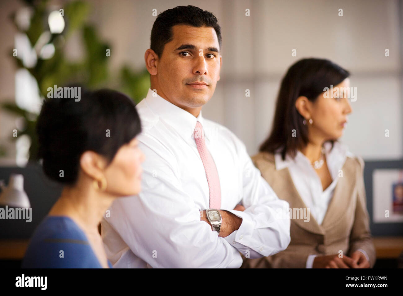 Porträt einer zuversichtlich, Mitte - Erwachsene Geschäftsmann, der mit seinen Armen neben zwei weiblichen Kollegen gekreuzt, während in einem Büro stehen. Stockfoto