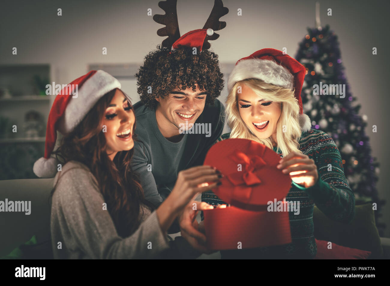 Fröhliche schöne junge Freunde Weihnachten zu Hause genießen, Geschenk und überraschend, was drin ist. Stockfoto