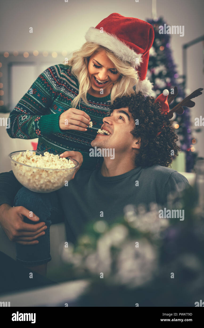 Paar in der gemütlichen warmen Pullover auf einem Weihnachten Silvester, lächelnd und Spaß miteinander essen Popcorn. Selektive konzentrieren. Stockfoto