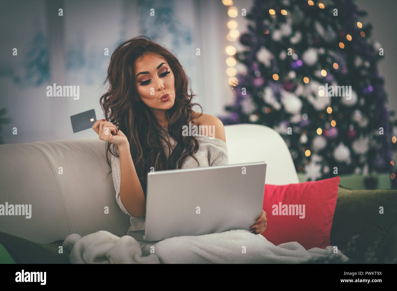 Fröhliche junge Frau in eine Decke gewickelt und Kaufen Weihnachtsgeschenke online zu Hause. Stockfoto