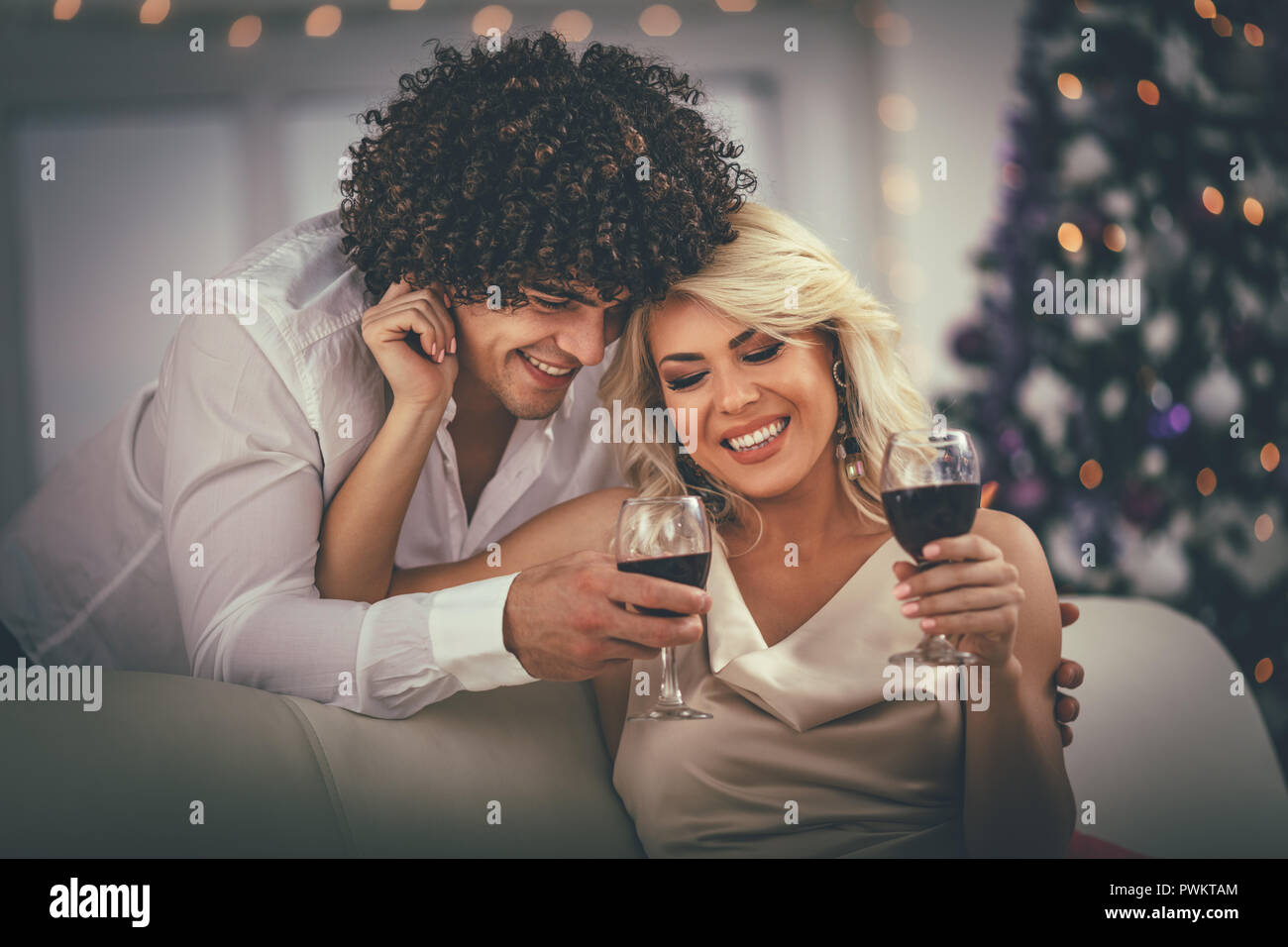 Junges Paar Weihnachten zu Hause feiern. Entspannen Sie sich mit einem Glas Rotwein, mit Decke auf dem Sofa in einer Wohnung abgedeckt. Stockfoto
