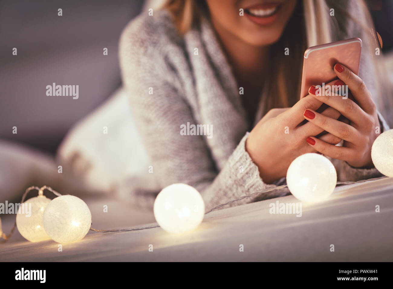 Nette junge lächelnde Frau mit Smartphone und während gemütliche Weihnachten Urlaub zu Hause ein Lächeln auf den Lippen. Stockfoto