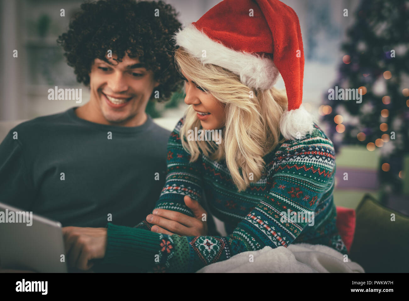 Fröhlicher junger Paare Entspannung zu Hause und online kaufen Weihnachtsgeschenke auf dem Laptop. Stockfoto