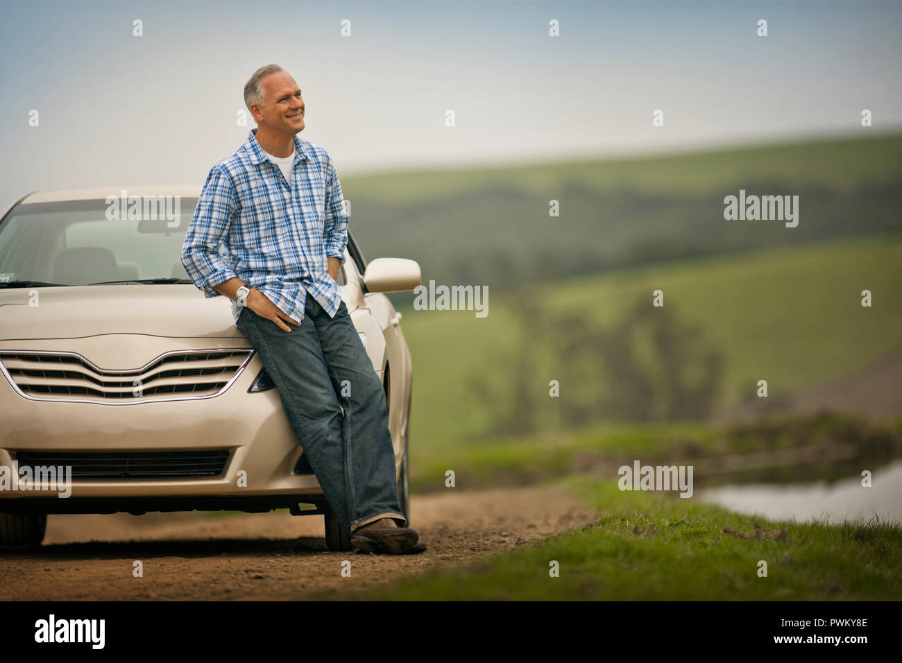 Lächelnd im mittleren Alter Mann lehnte sich auf der Motorhaube seines Autos. Stockfoto