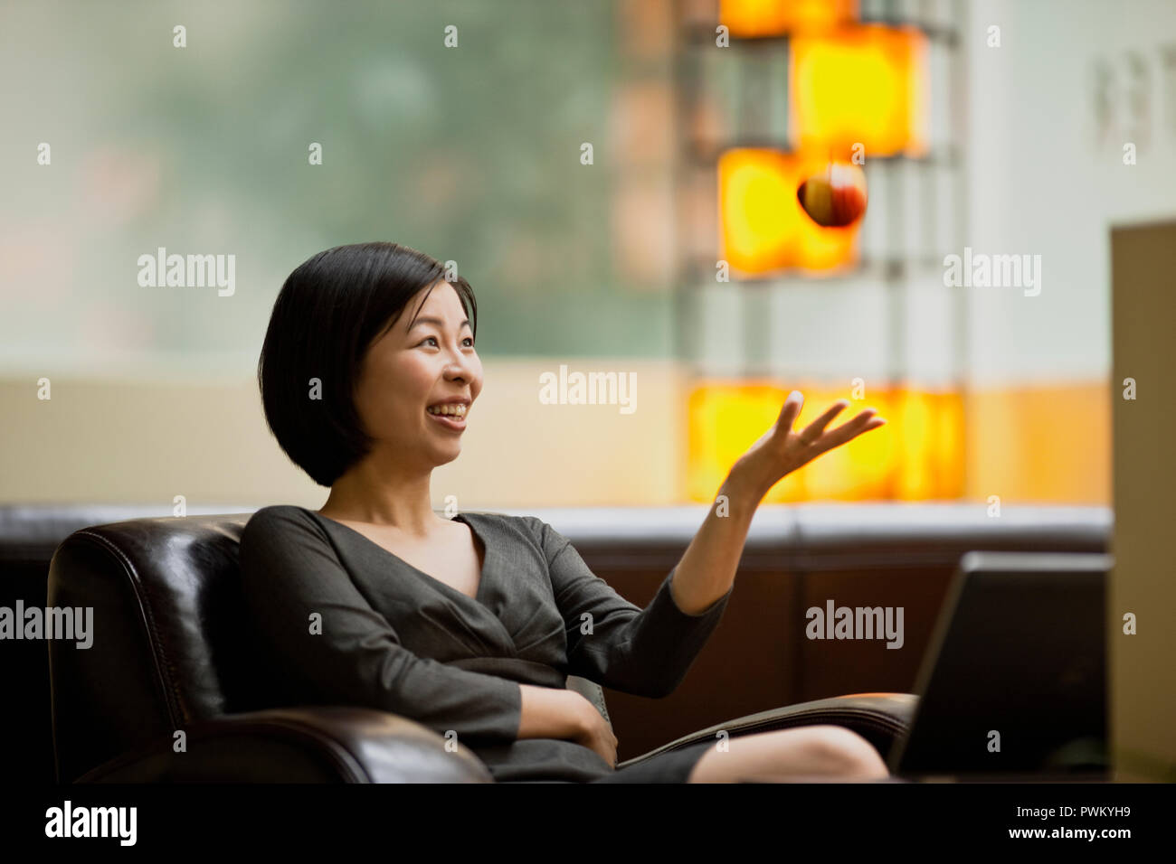 Frau sitzt auf einem Sofa in der Lobby werfen einen Apfel in die Luft. Stockfoto