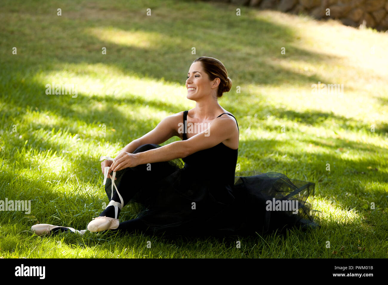 Mitte der erwachsenen Frau sitzen und Lächeln in einem Park beim Tragen eines Ballett Kostüm. Stockfoto