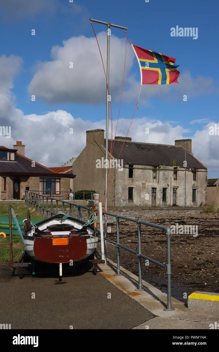 Ein sehr zerschlissenen Fahne von Orkney, Schottland, Fliegen im starken Wind in vom Pier in St. Mary's. Strahlend blauen Himmel, weiße Wolken, Boot, Gebäude, Ufer. Stockfoto