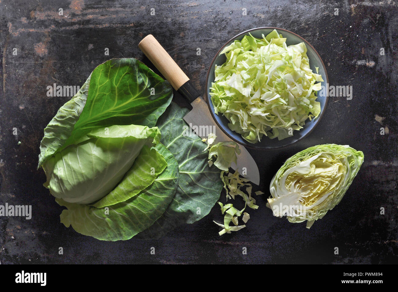 Spitzkohl, ganz, halbiert und in Scheiben geschnitten, in eine keramische Schüssel mit einem Messer auf einem schwarzen Backblech Stockfoto