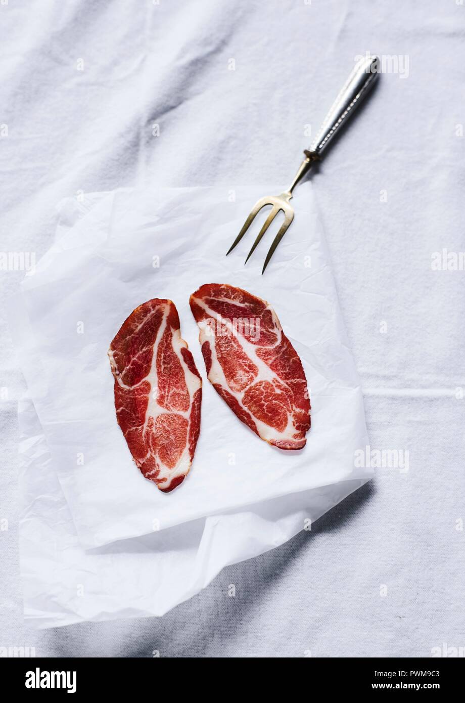Zwei Scheiben Wurst mit Fleisch Gabel auf einem Blatt Papier Stockfoto