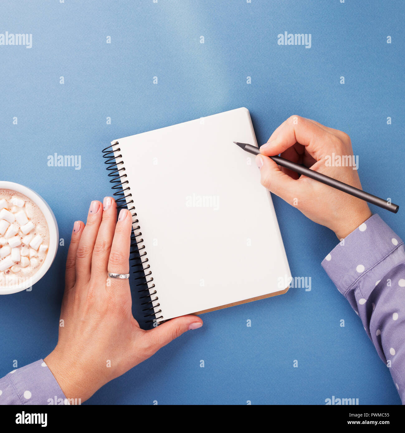 Woman's Hand schreiben im Notebook auf dem blauen Hintergrund. Ansicht von oben. Stockfoto
