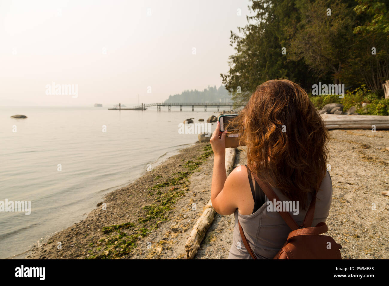 Eine brünette Frau nimmt ein Foto von der Dunst in der Umgebung von Vancouver 2018 Waldbrände. Stockfoto