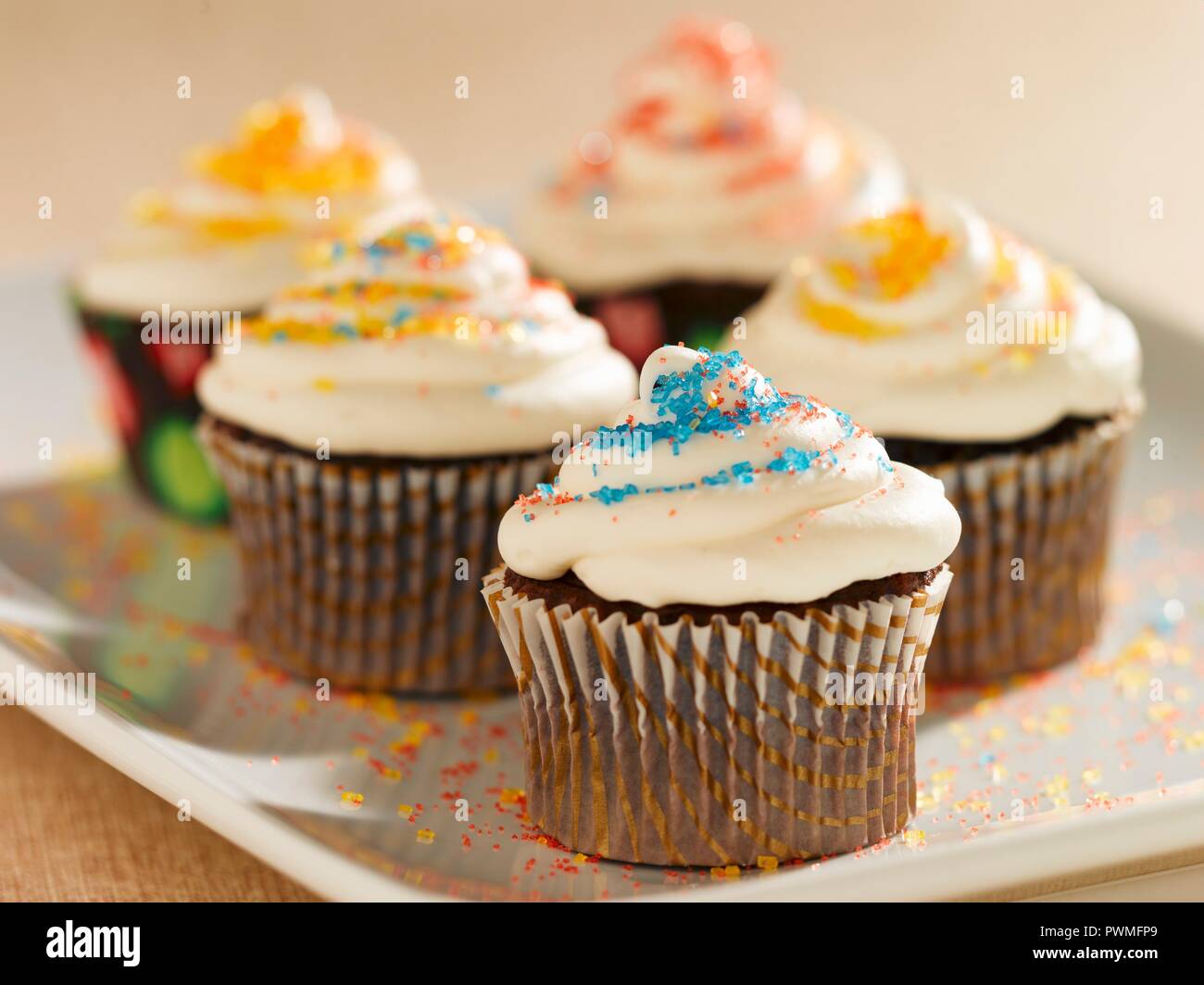 Schoko Cupcakes mit Vanille Glasur und bunten Zucker Kristalle; auf einer Platte Stockfoto