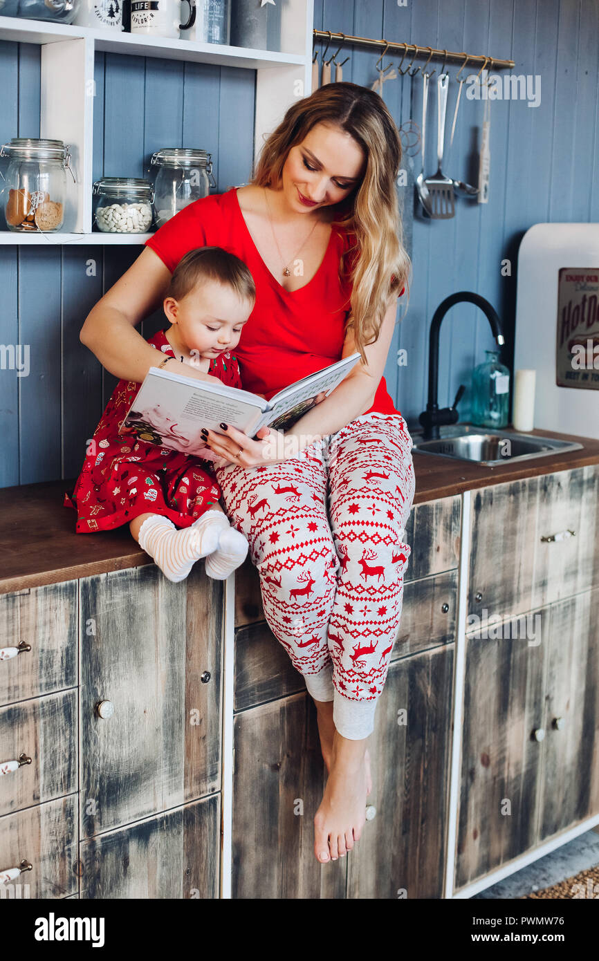 Schöne blonde Mutter mit Tochter sitzen gemeinsam in der Küche im  Schlafanzug und lächelnd. Kleines Mädchen mit Mama das Tragen der roten  Weihnachten Schlafanzug re Stockfotografie - Alamy